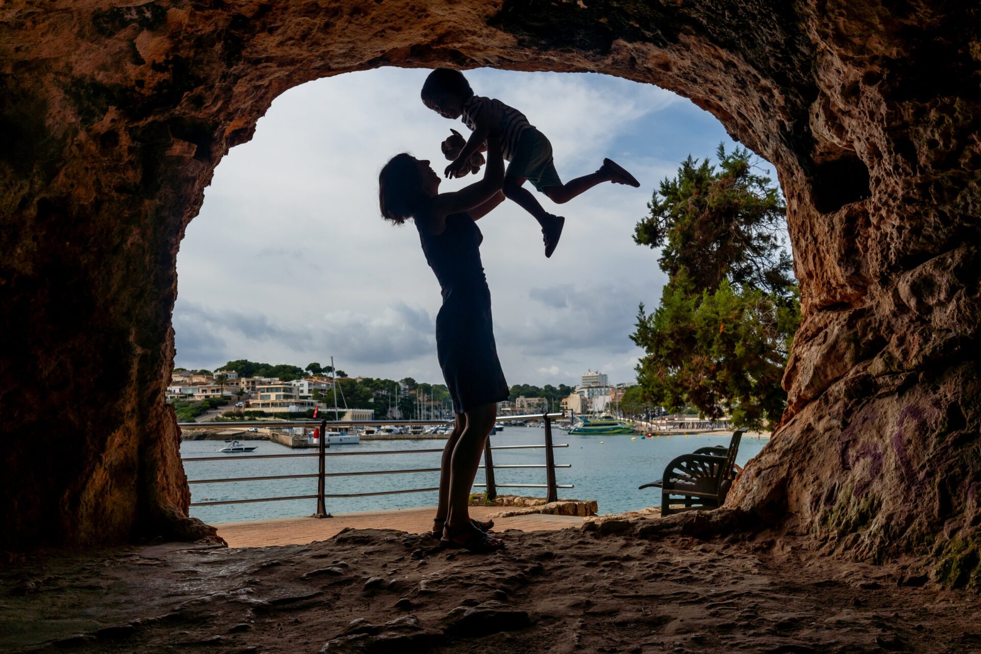 Mutter hebt Sohn in einer Höhle mit Blick auf den Hafen von Puerto Cristo auf Mallorca